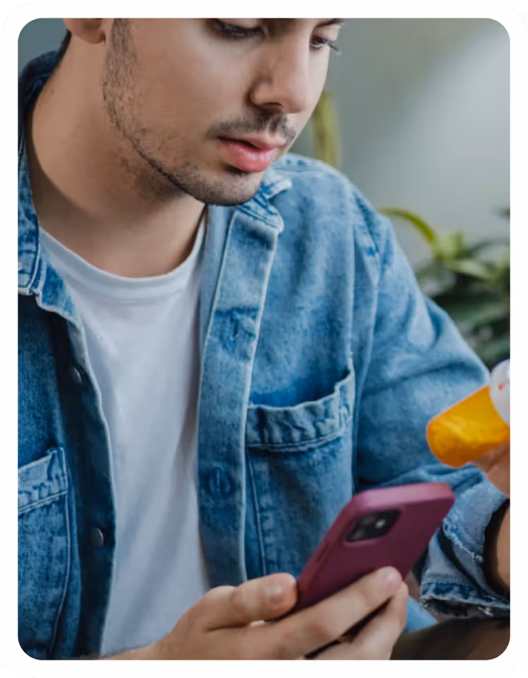 Man in denim shirt holding a smartphone, reading attentively.
